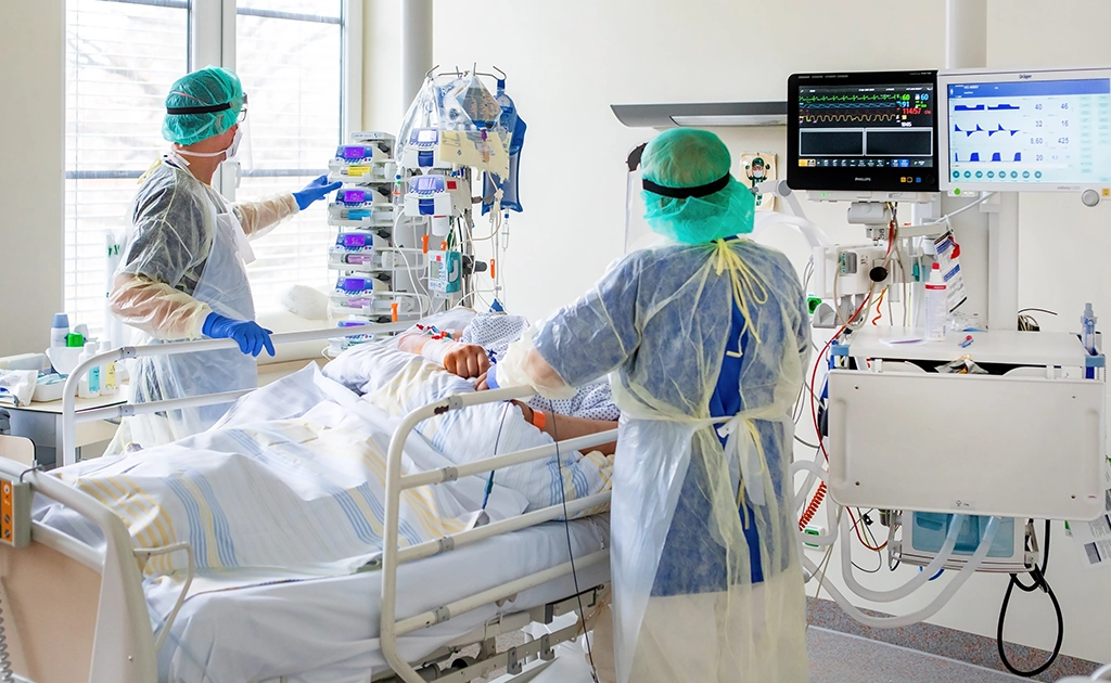 Patient im Krankenhausbett, medizinisches Personal in Schutzkleidung arbeitet mit Geräten (foto)