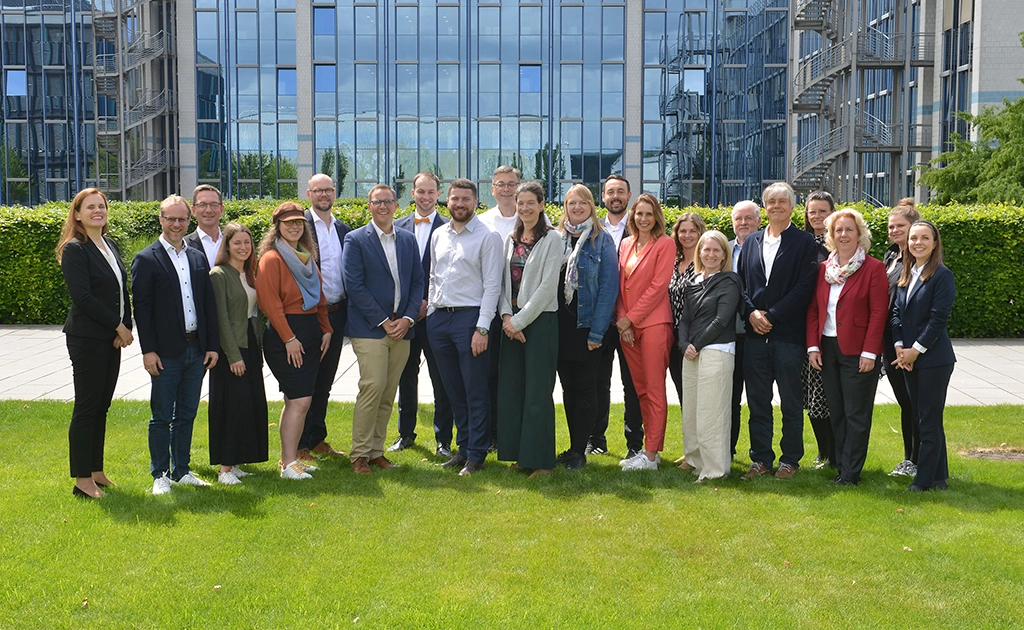 Group photo from the kick-off meeting on a green field with corporate headquarters in the background (photo)